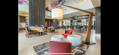 Modern lobby with red chairs, white ottomans, and a fireplace.