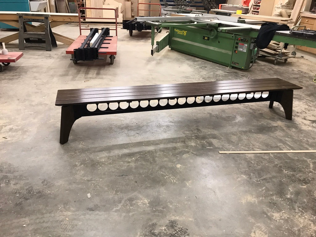 Long dark brown bench in a workshop setting with tools and equipment in the background.
